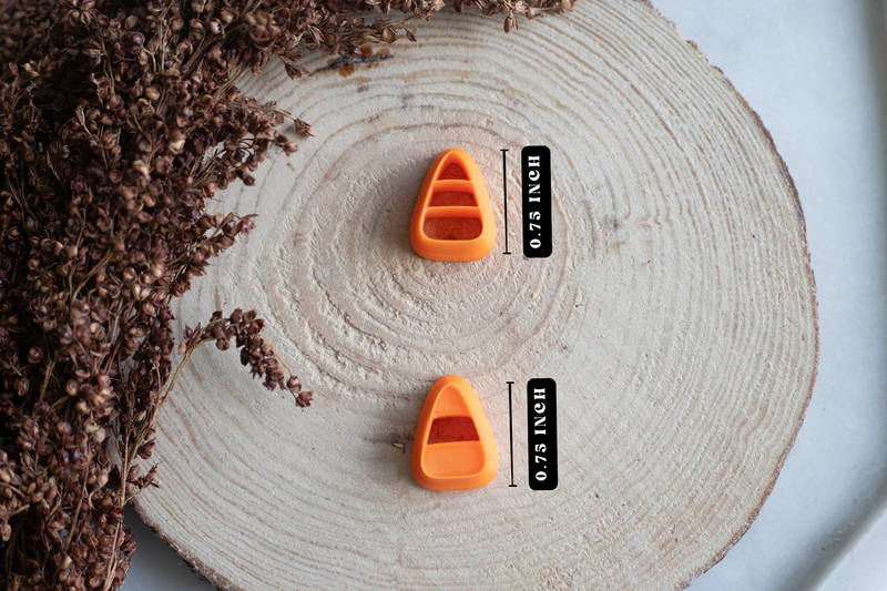 Two small orange boat-shaped measuring tools labeled 0.75 inches, arranged on a round wood slice with dried brown flowers at the side.