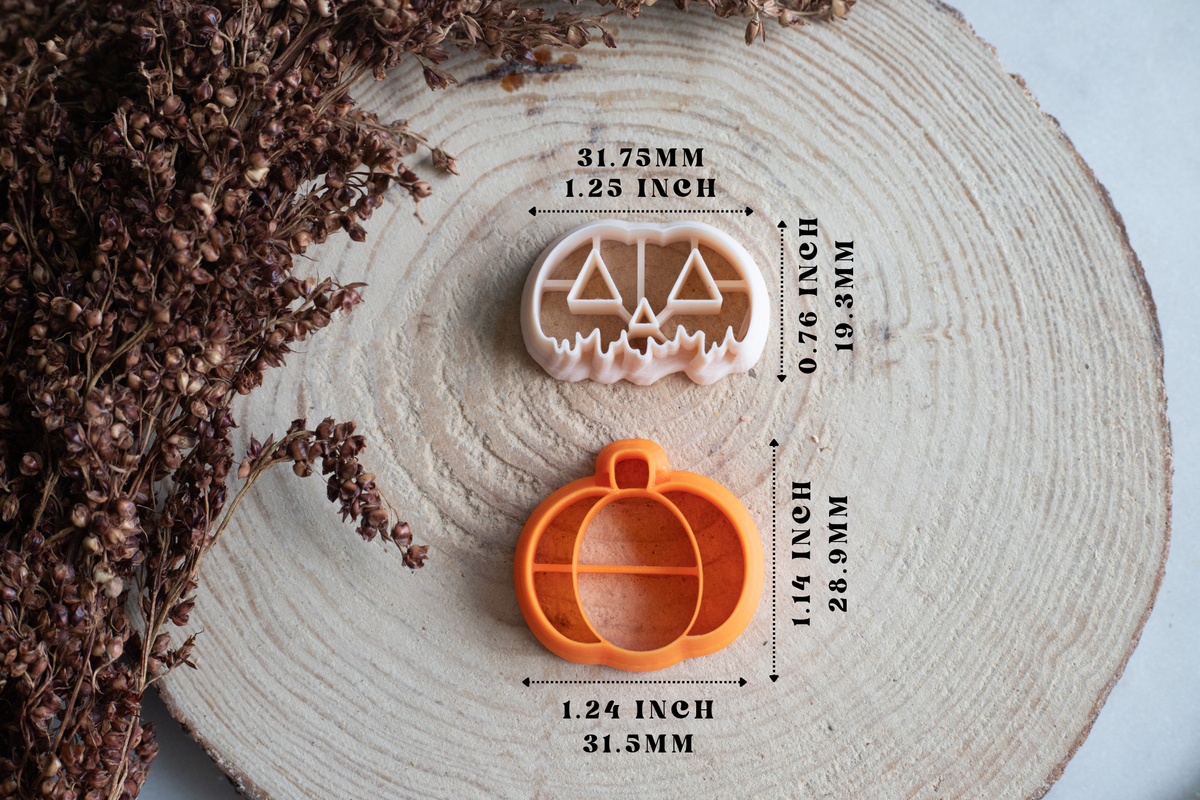 An orange pumpkin-shaped cookie cutter and a beige jack-o'-lantern cookie cutter are displayed on a round wood slice with dried flowers. Black measurement lines and text indicate the dimensions of both cutters.